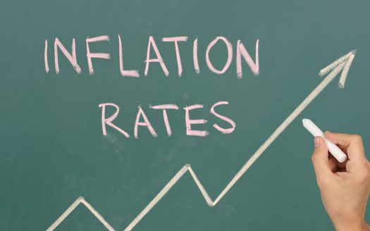 "inflation rate" is written in a green board with a hand holding the chalk